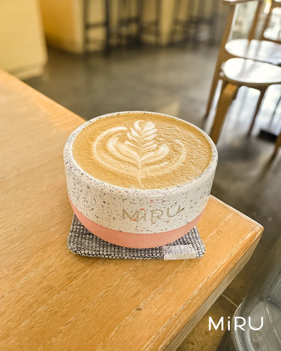 Latte MiRU dengan latte art daun di cangkir MiRU bermotif di atas meja kayu