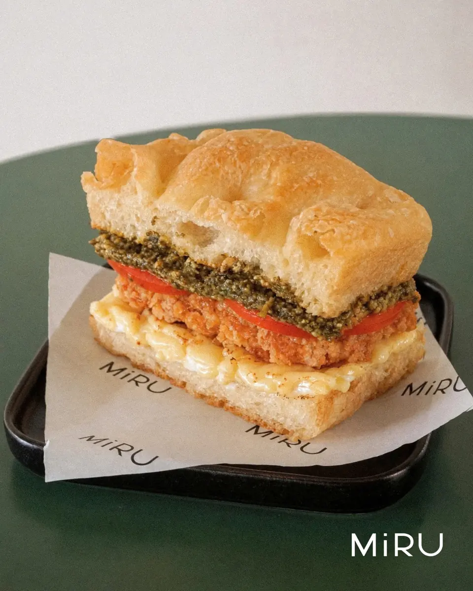 Sandwich focaccia MiRU dengan pesto, tomat, dan keju di atas kertas bermerek MiRU